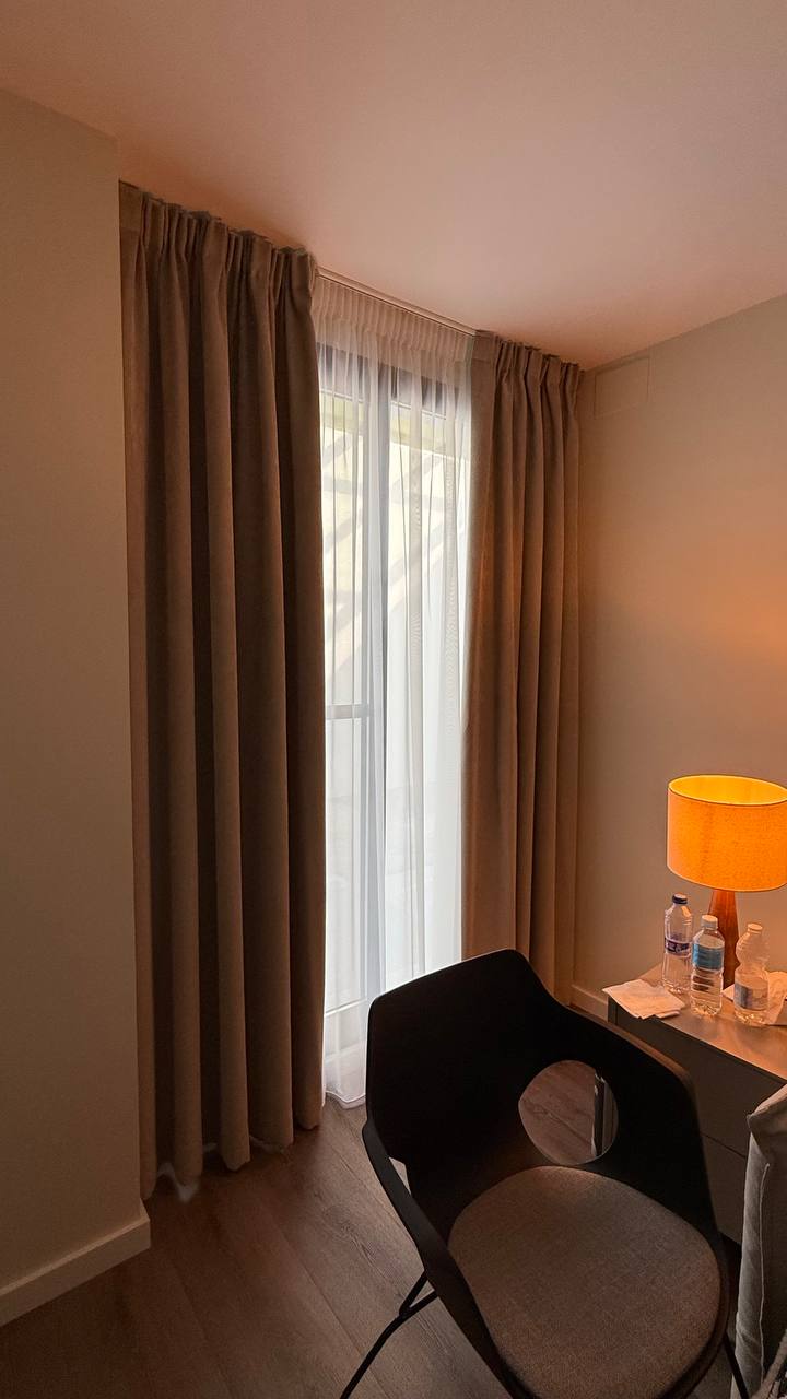 Cortina opaca beige con visillo blanco en una ventana estrecha de dormitorio
