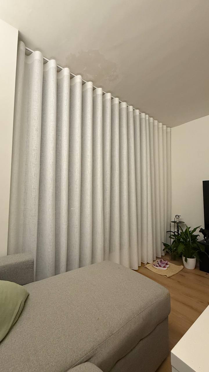 Cortina de lino claro con caída ondulada cubriendo una pared completa junto al sofá